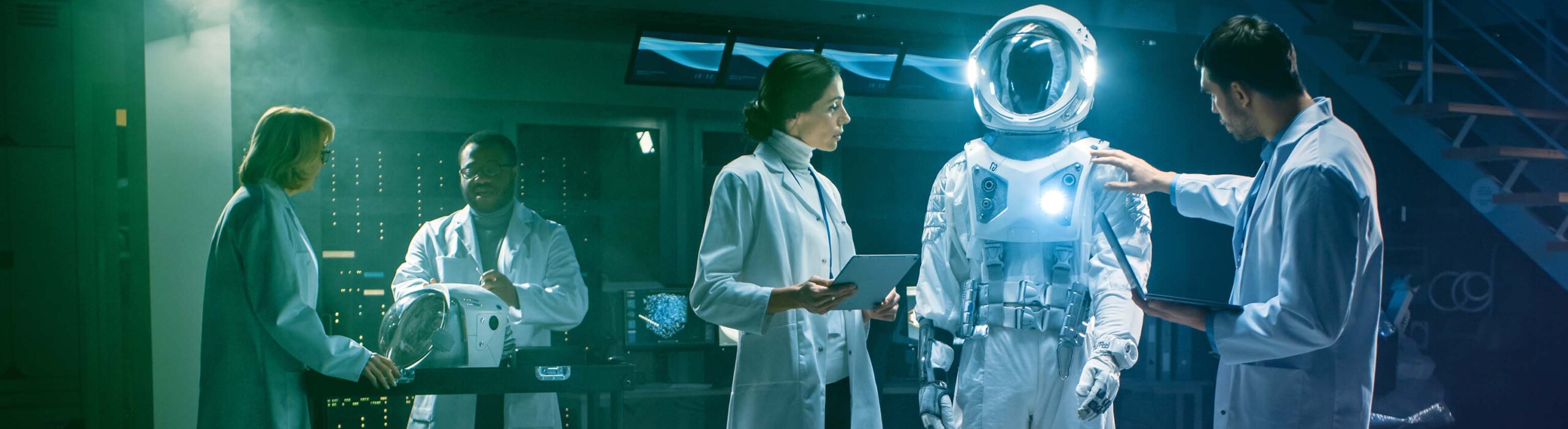 Team of Aerospace Engineers Design New Space Suit Adapted for Galaxy Exploration and Travel. Group of Scientists Wearing White Coats have Discussion, Use Computers. Constructing Astronaut Helmet